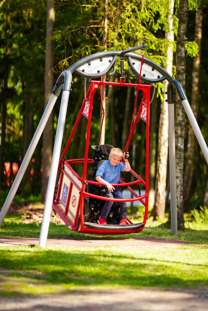 Gutt i rulletsol som sitter i huskestativ som er tilpasset for rullestol. Foto